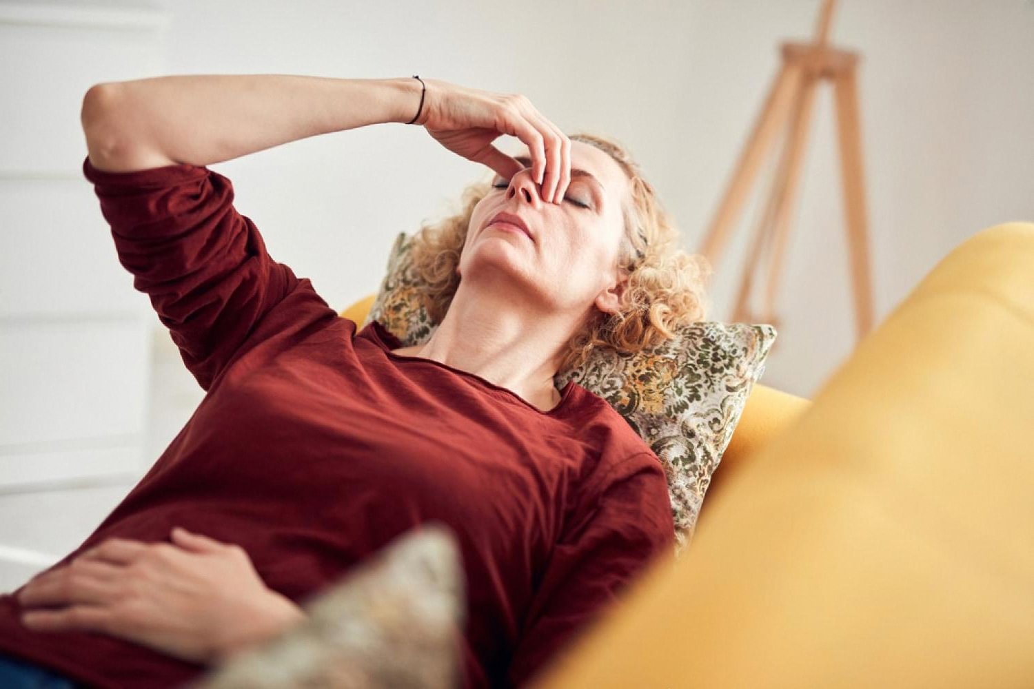 Woman lying on a sofa holding her forehead, suffering from persistent nausea and fatigue