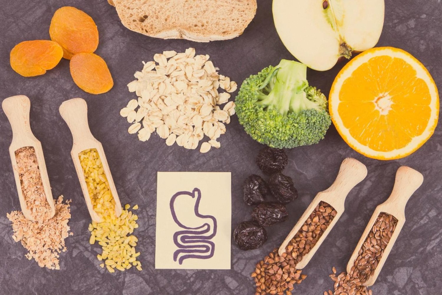 Fibre-rich foods including oats, fruit and seeds arranged around a stomach illustration for digestive health
