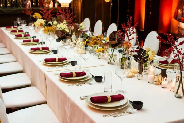 Long banquet table with premium event rental setup in Dubai featuring burgundy napkins, gold ring holders and floral centrepieces